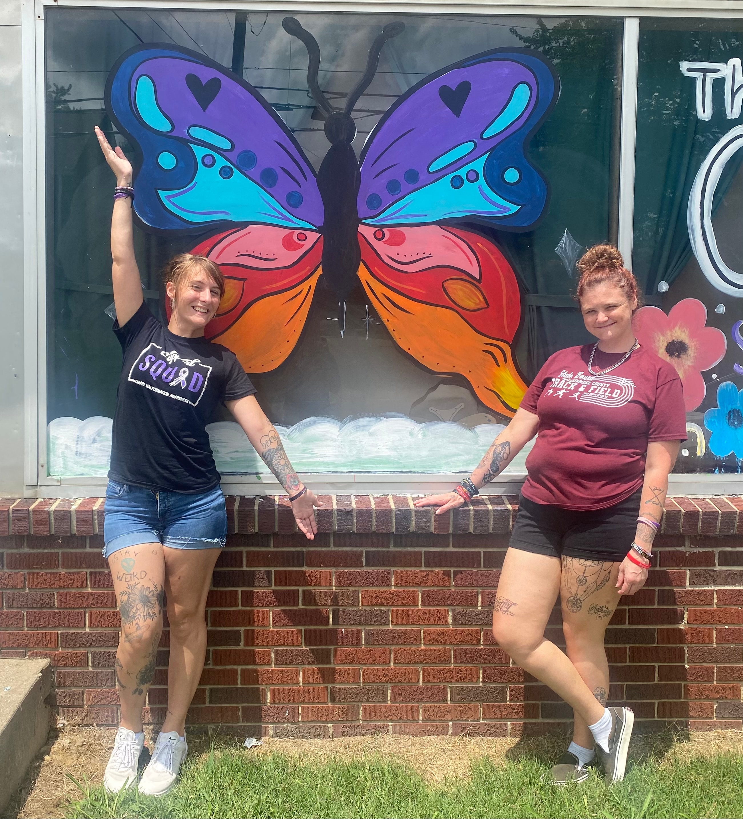 Two Gift House women posing in front of a colorful butterfly mural