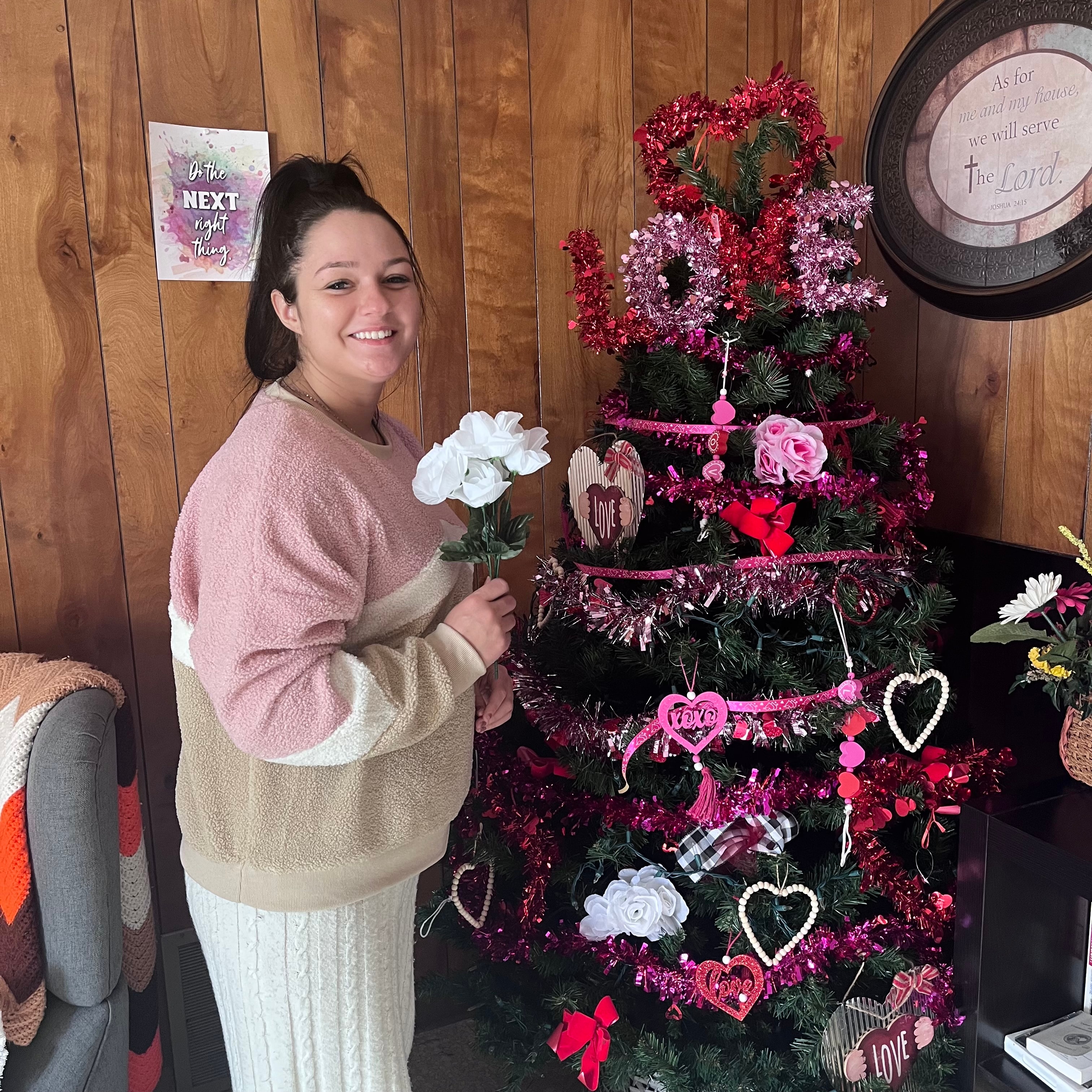 Gift House resident smiling beside a decorated Valentine's tree inside the home